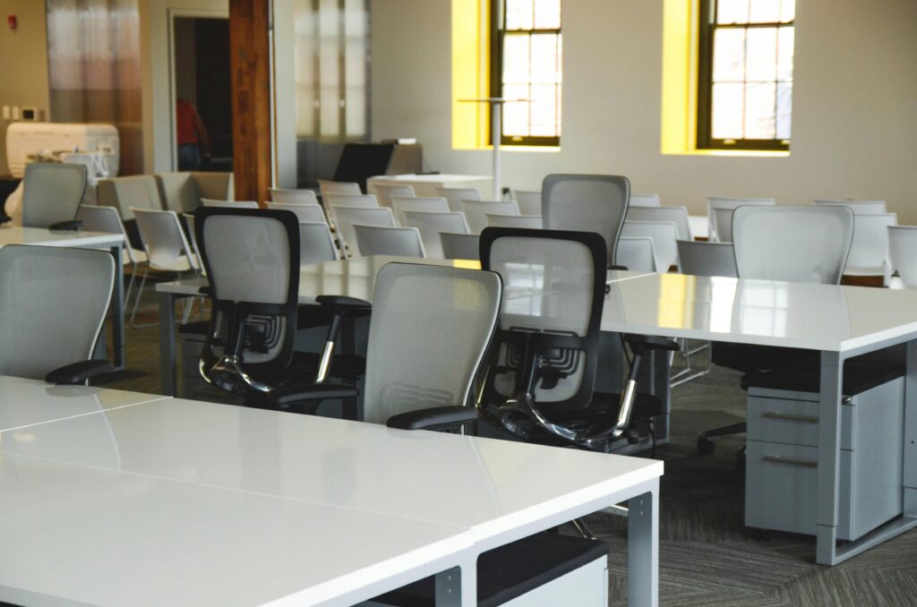 Spacious open office workspace with desks, chairs, and natural lighting.